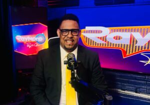 Raymond-podcast-host-smiling-in-suit-with-microphone
